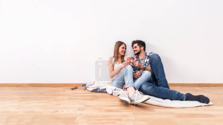 Photo for Young couple sitting on the floor of empty flat celebrating with champagne - Royalty Free Image