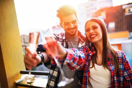 Téléchargez les photos : Jeune couple décontracté célébrant avec champagne sur la terrasse de l'appartement - en image libre de droit