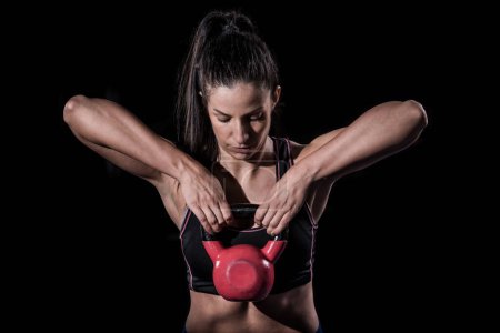 Photo for Woman bodybuilder lifting kettle bell isolated over black background - Royalty Free Image