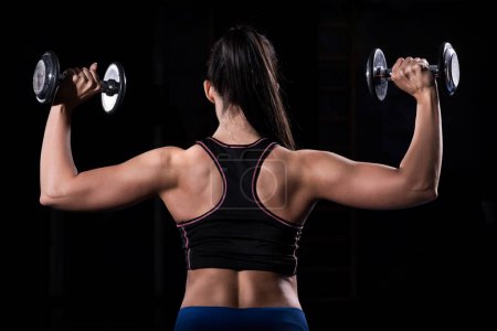 Photo for Woman bodybuilder lifting dumbbells isolated over black background - Royalty Free Image