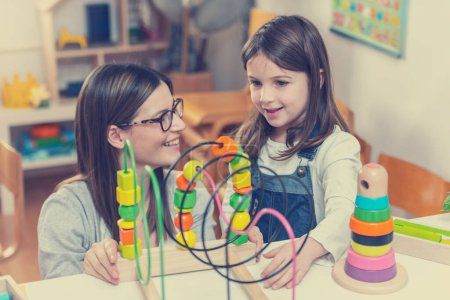 Téléchargez les photos : Professeur de maternelle regardant l'enfant jouer avec des jouets didactiques colorés à l'intérieur - préscolaire - en image libre de droit