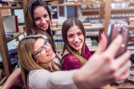 Photo for Group of smiling female students taking selfie at school library - Royalty Free Image