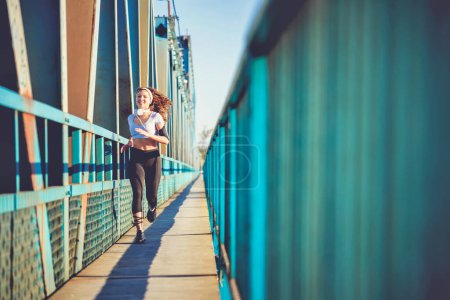 Foto de Joven corredora de polainas corriendo por el puente de la ciudad - Imagen libre de derechos