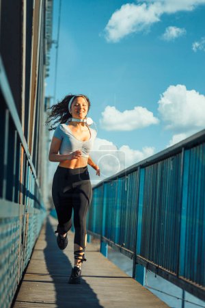Photo for Young woman runner in leggings running on the bridge in the city - Royalty Free Image