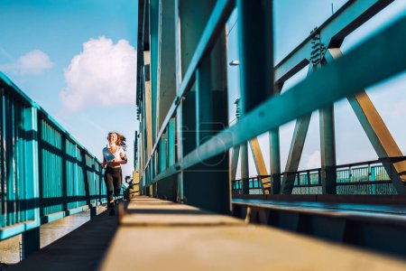 Téléchargez les photos : Jeune femme coureuse en legging courant sur le pont de la ville - en image libre de droit
