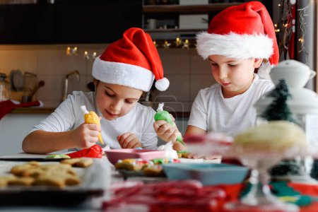 Foto de Dos niños felices decorando galletas para las vacaciones en casa - Imagen libre de derechos