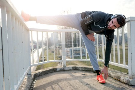 Photo for Jogger stretching before exercise and listening music outdoors - Royalty Free Image