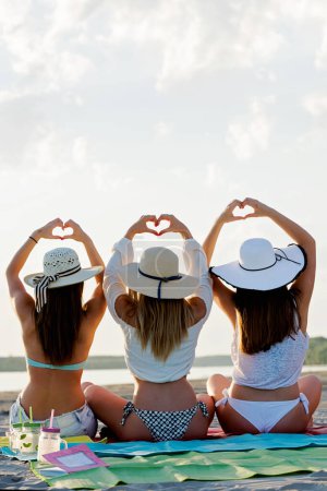 Foto de Chicas con sombreros en la playa de verano mostrando corazones - Imagen libre de derechos