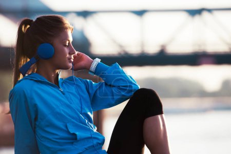 Photo for Young woman jogger resting listening music by the river - Royalty Free Image