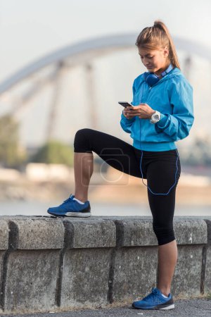 Téléchargez les photos : Jeune femme jogger en utilisant smartphone au bord de la rivière - en image libre de droit