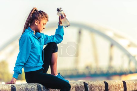 Foto de Joven corredora con botella de agua junto al río - Imagen libre de derechos