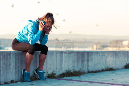 Téléchargez les photos : Jeune femme jogger au repos écouter de la musique au bord de la rivière - en image libre de droit