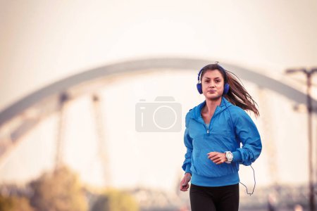 Téléchargez les photos : Jeune femme joggeuse courant au bord de la rivière le matin - en image libre de droit