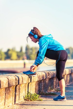 Photo for Young woman jogger tying shoelaces by the river - Royalty Free Image