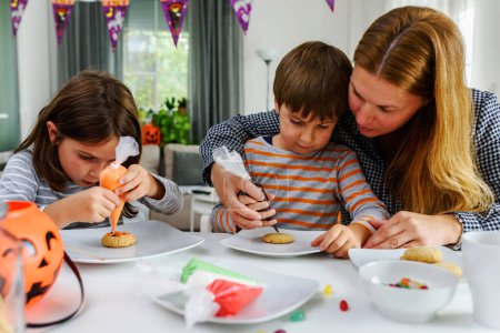 Foto de Madre con niños decorando galletas para la celebración de Halloween - Imagen libre de derechos