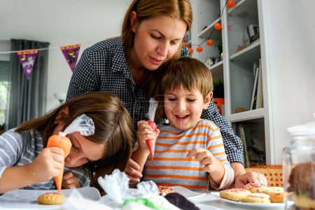 Téléchargez les photos : Mère avec des enfants décorant des biscuits pour la célébration d'Halloween - en image libre de droit