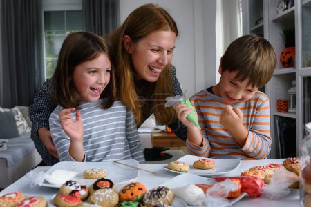 Foto de Madre con niños decorando galletas para la celebración de Halloween - Imagen libre de derechos