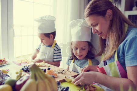 Photo for Happy young kids with their mother in the kitchen - preparing a healthy fruits snacks - Royalty Free Image