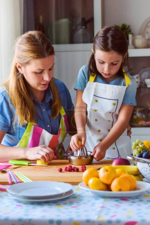 Téléchargez les photos : Mère et fille préparant des fruits pour la salade - en image libre de droit