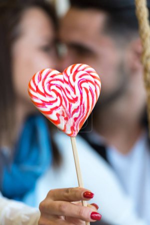 Foto de Pareja joven enamorada en columpios con corazón de caramelo - Imagen libre de derechos
