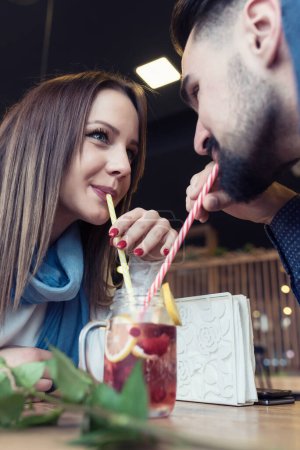 Photo for Young Love Couple in Caf Drinking from the same Glass with Straws - Royalty Free Image
