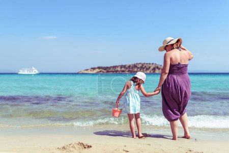 Téléchargez les photos : Vue arrière d'une mère et d'une fille debout sur une plage d'émeraude parfaite - en image libre de droit