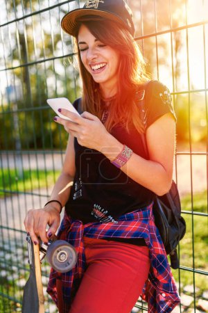 Téléchargez les photos : Mignonne fille urbaine tenant longboard dans skate park avec téléphone - en image libre de droit