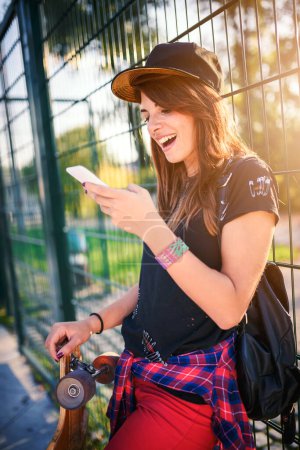Photo for Cute urban girl holding longboard in skate park with phone - Royalty Free Image