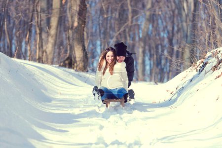 Joven pareja juguetona divertirse trineo abajo nieve cubierta colina
