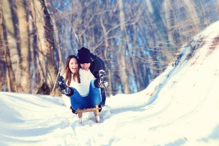 Photo for Young playful couple having fun sledging down snow covered hill - Royalty Free Image