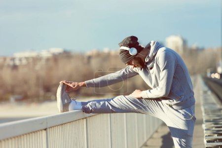 Photo for Young athlete man stretching his muscles before running on bridge. Exercising, Jogging, Sport, extreme. - Royalty Free Image