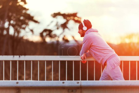 Photo for Man runner taking a break after intensive training outdoors, listening music - Royalty Free Image