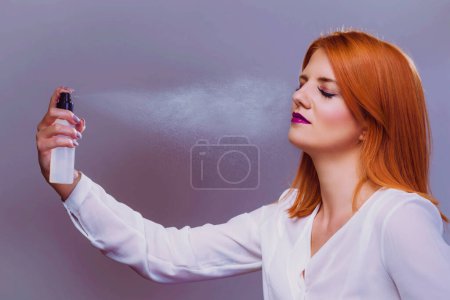 Téléchargez les photos : Belle femme appliquant une pulvérisation de réglage de maquillage hydratant sur le visage - en image libre de droit