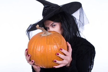 Téléchargez les photos : Belle jeune sorcière en costume noir d'Halloween tenant citrouille - en image libre de droit