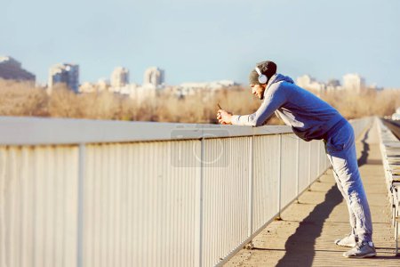 Téléchargez les photos : Homme de jogging urbain prenant frein écouter de la musique sur son téléphone intelligent - en image libre de droit