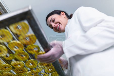 Foto de Sonriente técnico de alimentos femenino que trabaja en la máquina deshidratadora de secador de alimentos - Imagen libre de derechos
