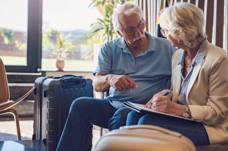 Photo for Senior couple checking into a hotel. Elderly couple sitting in a hotel lobby filling in forms. Older people traveling. - Royalty Free Image