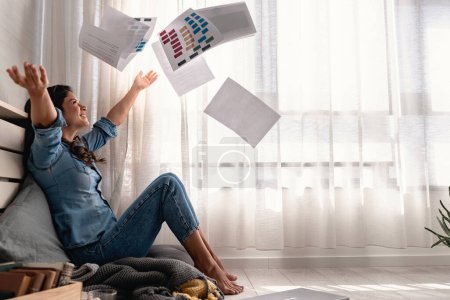 Téléchargez les photos : Heureuse jeune femme d'affaires indépendante assise sur le sol à la maison jetant des papiers dans les airs après avoir résolu un problème - en image libre de droit