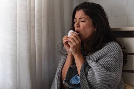 Foto de Mujer joven en casa limpiándose la nariz, estornudando, resfriada, gripe, alergias. Tratando de calentar. - Imagen libre de derechos