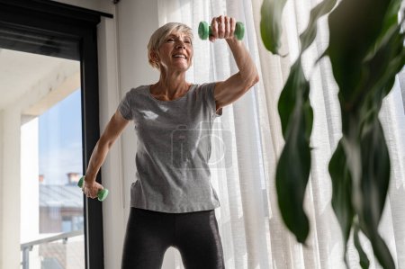 Foto de Sonriendo hermosa mujer mayor instructor de salud haciendo ejercicios con pesas - Imagen libre de derechos