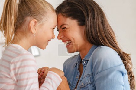 Téléchargez les photos : Un moment joyeux et affectueux se déroule comme une mère gaie et sa fille partagent des sourires chaleureux, câlins et s'amuser ensemble. - en image libre de droit