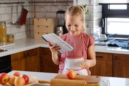 Téléchargez les photos : Portrait d'une jolie petite fille dans une cuisine maison avant de préparer une tarte aux pommes - en image libre de droit