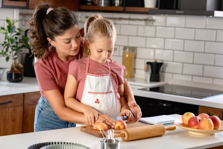 Photo for Beautiful happy mother and daughter preparing an apple pie at home kitchen. Autumn fun family activities - Royalty Free Image