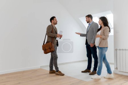 Foto de Hombre y su esposa embarazada, hablando con un agente de bienes raíces visitando apartamento en venta o en alquiler. Futuros padres comprando un apartamento. Concepto inmobiliario - Imagen libre de derechos
