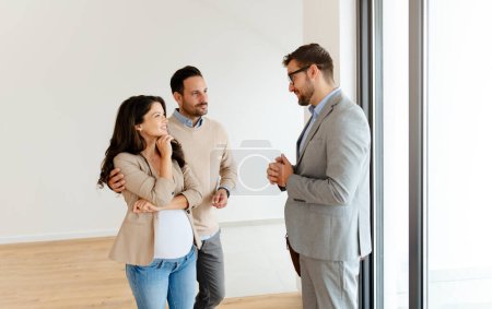 Photo for Man and his pregnant wife, talking with a real-estate agent visiting apartment for sale or for rent. Future parents buying an apartment. Real estate concept - Royalty Free Image