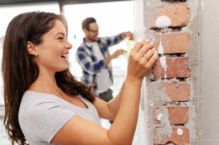 Una pareja joven, hermosa y alegre, compuesta por un hombre y su esposa embarazada, están midiendo las paredes, como parte de su nuevo proyecto de renovación del hogar