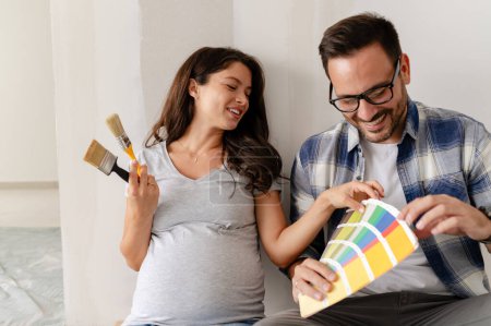 Photo for Pregnant woman and her husband choosing paint color for painting walls at new apartment - Royalty Free Image