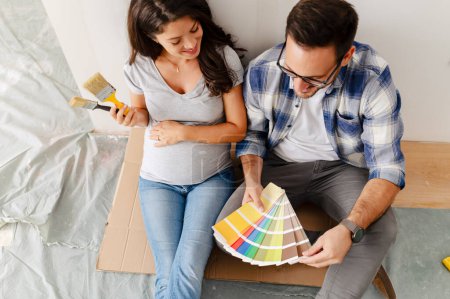 Téléchargez les photos : Femme enceinte et son mari choisissant la couleur de peinture pour peindre les murs dans un nouvel appartement - en image libre de droit