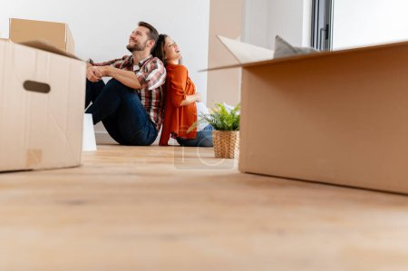 Photo for Couple sitting on floor with cardboard boxes at home moving to new house - Royalty Free Image