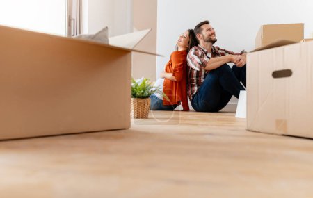 Photo for Couple sitting on floor with cardboard boxes at home moving to new house - Royalty Free Image